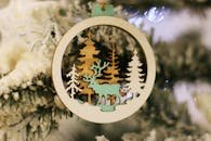 Close-up of a rustic wooden ornament featuring a reindeer, hanging on a snowy Christmas tree branch.